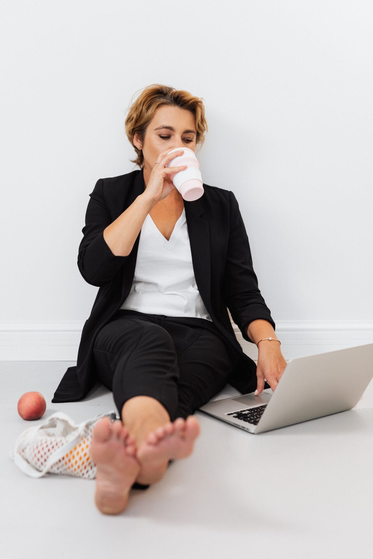 Vrouw in zakelijke kleding neemt een moment voor zichzelf met koffie en laptop, BalansInzicht Preventiescan voor energie en werkplezier.
